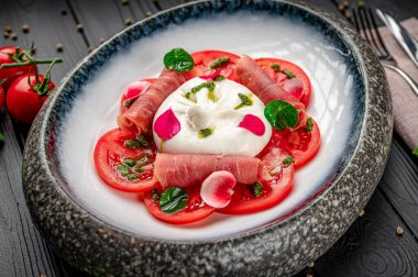 Taze mozzarella, domates ve otlarla servis edilir. Bir tabak taze mozarella peyniri, domates ve otlar garnitürle servis edilir..