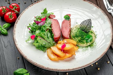 Tabağında salata, et ve meyve olan bir restoranda servis edilen yemek. Bir yemek, salatayla dilimlenmiş et, pişmiş meyve ve tabakta yeşil sos içerir..