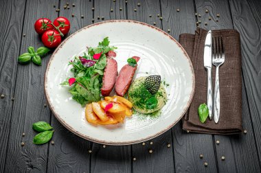 Et, salata, şeftali ve kır sofrasında otlarla dolu lezzetli bir yemek. Bir yemekte et dilimleri, salata, şeftali ve ahşap bir masada yeşil otlar bulunur..