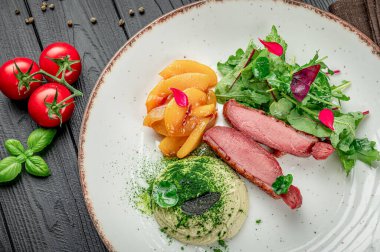 Tabakta et, salata, meyve ve domatesli sos olsun. Tabakta et, yeşillik, dilimlenmiş meyve ve sos, ahşap bir masada domatesler var..