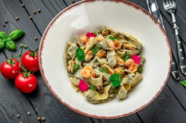 Beyaz kasede taze domatesle servis edilen karidesli makarna. Bir kasede karides, fesleğen ve süslemeli makarna var. Taze domatesler tabağın etrafını sarmış karanlık bir masada..