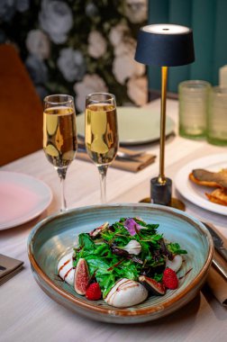 Akşam bir restoranda salata ve içeceklerle nefis bir yemek düzeni. İki bardak şampanya, bir kase salatanın yanında oturuyor ve akşam bir restoranda masada meyveler var..