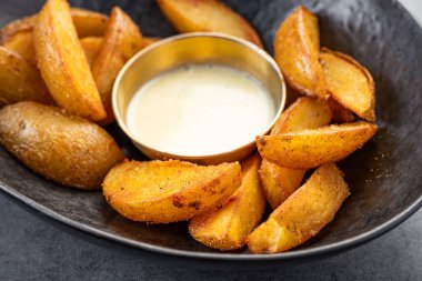 Yuvarlak bir kasede sosla servis edilen çıtır patatesler. Bir tabak altın patates dilimleri küçük bir kase kremalı sosun yanında atıştırmak için durur..