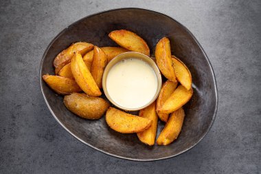 Sıradan bir yemek ortamında sosla servis edilen çıtır patatesler. Çıtır patatesler, küçük bir kase sosun yanında bir kaseye konur..