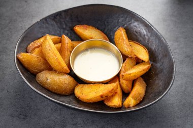 Siyah bir kaseye batırılmış sosla servis edilen sıcak patates dilimleri. Patates kamaları düzgün bir şekilde ortada küçük bir fincan sosla bir kaseye yerleştirilir..