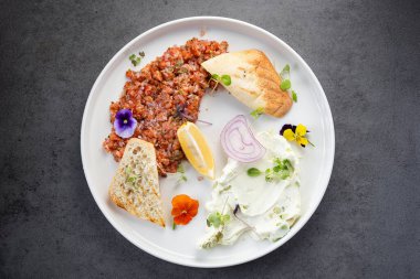 Bir tabak doğranmış et, ekmek, soğan ve beyaz tabakta otlar. Bir yemek, ekmek, limon, soğan ve beyaz bir tabakta sunulan doğranmış eti gösterir..