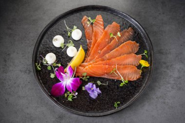 Siyah bir tabakta sunum için taze somon ve bitkiler. Somon filetoları siyah bir tabakta hazırlanır. Bitkiler ve yenilebilir çiçeklerle süslenir..