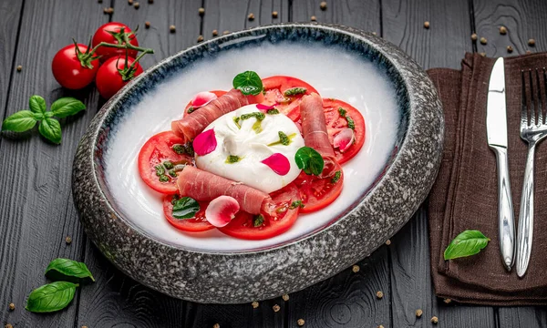 Koyu ahşap bir masada domatesli, peynirli ve jambonlu lezzetli bir yemek. Kırmızı domatesler ahşap bir masanın ortasında jambon ve peynirle düzenlenir..