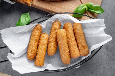 Mutfak ortamında fesleğen yapraklarıyla servis edilen sıcak çerez çubukları. Bir sepette altın atıştırmalık çubuklar var. Taze fesleğen yaprakları yakınlarda..