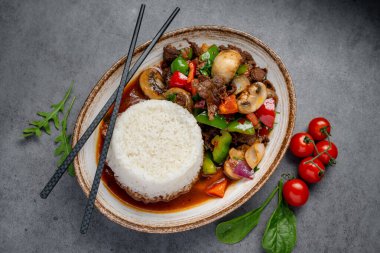 Tabakta servis edilen sebzeli ve pirinçli biftek kızartması. Renkli sebzelerle bir tabak sığır kızartması ve çubuklu bir tabak beyaz pirinç..