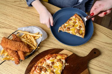 İnsanlar pizza, tavuk şeritleri ve patates kızartması olan bir masada yemek yemekten hoşlanırlar. İnsanlar yemek saatinde ahşap bir masada pizza, tavuk ve patates kızartması paylaşıyor..