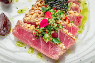 Restoran ortamında yeşil sos ve otlarla servis edilen ton balığı tabağı. Tabakta yeşil soslu ve otlu ton balığı bifteği var. Yakınlarda pancar kökü parçaları var..