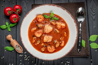 Karidesli deniz ürünleri güveci ve karanlık bir masada domates suyunda istiridye. Bir kase içinde karides ve domates suyunda midye olan deniz ürünleri güveci barındırır..