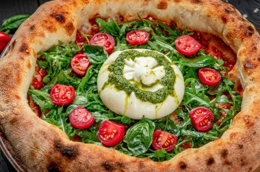 Restoran ortamında burrata, roka ve domatesli taze pizza. Büyük bir pizza üzerine taze burrata peyniri, roka ve vişneli domates konur..