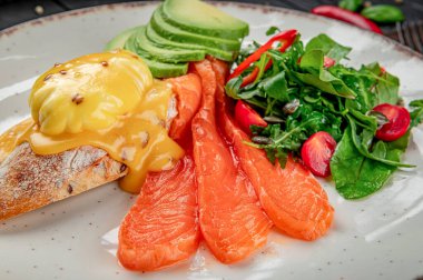 Avokado, salata ve bir tabakta servis edilen Hollandaise soslu füme somon. Tabakta füme somon, avokado ve yeşil biberli bir salata var..
