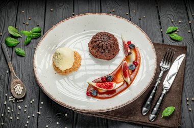 Çikolatalı pasta, dondurma ve masada servis edilen taze meyveli tatlı tabağı. Bir tatlı tabağında, ahşap bir masada servis edilen dondurmalı ve meyveli çikolatalı pasta ve çatal bıçaklarla servis edilir..