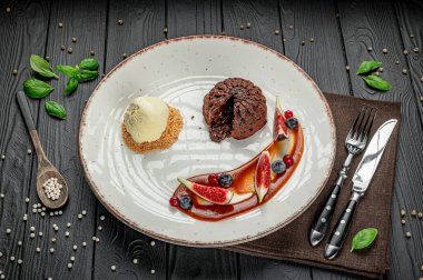 Lokantada beyaz bir tabakta servis edilen dondurmalı çikolatalı tatlı. Çikolatalı bir tatlı beyaz bir tabakta bir kepçe dondurmanın yanında oturur..