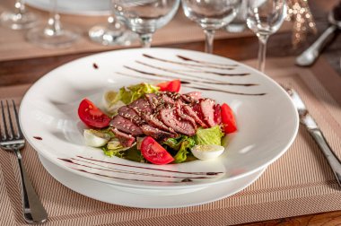 Dilimlenmiş et, salata ve domatesli yemek. Domatesli salata yatağında dilimlenmiş et yemek masasında eğlenmeye hazır..
