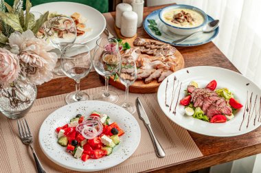 İçkiler ve çatal bıçaklarla ahşap bir masada servis edilen çeşitli yemekler. Salata ve et de dahil olmak üzere farklı yemekler, gözlüklü ve çatal bıçaklı ahşap bir masada düzenlenir..