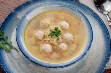 Köfteli çorba ve ahşap bir masada mavi bir kasede sebzeler. Bir kasede köfte, sebze ve otlarla dolu bir çorba var..