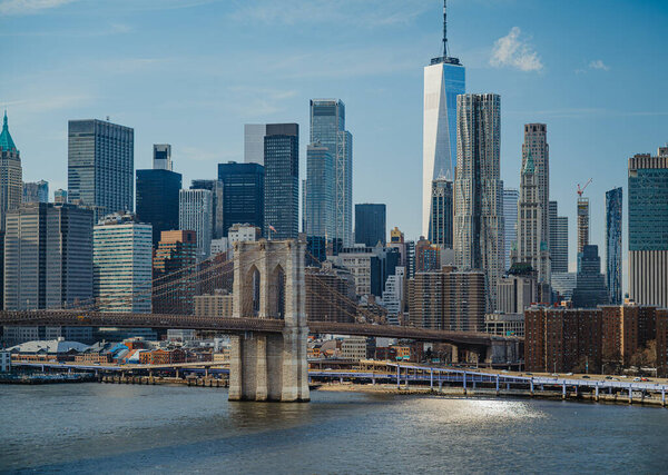 City skyline view with bridges and buildings under blue sky in New York. Tall buildings stand close to the water with a bridge connecting parts of the city on a bright day.