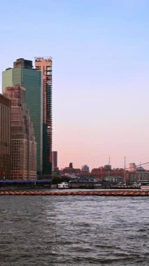 Brooklyn Köprüsü ve tekneler gün batımında. Köprü siluetleri, marina botları ve pastel gökyüzü ile doğu nehri boyunca akşam manzarası.