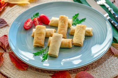 Lezzetli börekler mavi bir tabakta taze domateslerle servis ediliyor. Çeri domatesler ve yeşilliklerle mavi bir tabakta taze yapılmış börekler..