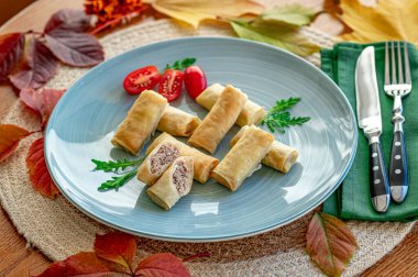 Mavi bir tabakta vişneli domatesle servis edilen taze fırınlanmış rulo. Bir tabak kiraz domatesleri ve yeşil yaprakların yanında fırında rulo gösteriyor..
