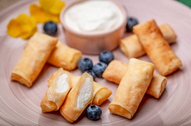 Krem peynirli lezzetli börekler ve tabakta taze yaban mersini. Krem peynirle dolu taze tatlı ruloları bir tabakta düzenlenir..