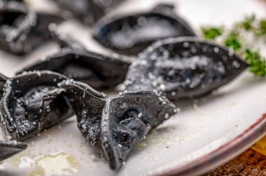 Eşsiz bir yemek deneyimi için tuzlu ve otlu bir tabakta servis edilen siyah makarna. Siyah makarna, bir tabak tuz serpiştirilip otlarla süslenir..