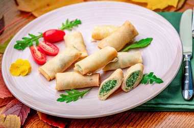 Tahta bir masada, üzerinde bitki ve kiraz domatesleriyle servis edilen börekler. Yumurtalı börekler hafif bir tabakta, otlar ve ahşap bir masada vişneli domateslerle düzenlenir..