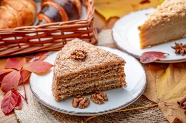 Ahşap bir masada kruvasanla servis edilen lezzetli katmanlı pasta. Beyaz bir tabakta fındıklı ve sonbahar yapraklı bir pasta servis edilir..