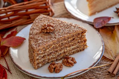 Ev yapımı, fındıklı kek ve sıcak bir tabakta sonbahar yaprakları. Bir dilim katmanlı kek, ceviz ve sonbahar yapraklarıyla dolu bir tabakta duruyor..