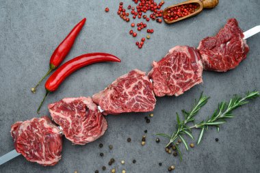 Gri bir yüzeyde acı biber ve baharatlı taze et şişleri. Şişler taze et parçalarıyla birlikte kırmızı biber ve baharatları gri bir yüzeyde tutar..