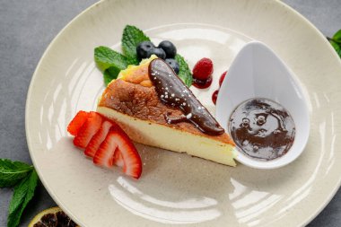 Tabakta servis edilen çikolata ve taze böğürtlenli leziz peynirli kek dilimi. Bir dilim cheesecake, etrafında çikolata sosu ve taze böğürtlen olan bir tabakta duruyor..