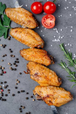 Yemek pişirmek için gri bir yüzeye domatesli tavuk kanadı ve otlar. Tavuk kanatları gri bir yüzeye yerleştirilir. Hazırlık ve pişirme için domates, bitki ve baharatlarla birlikte..