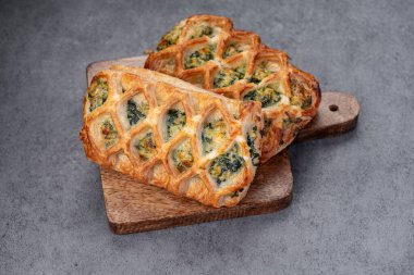 Tahtada ıspanaklı taze pişmiş hamur işleri. Ispanakla dolu iki altın sarısı hamur işi mutfak ortamında tahta bir kesme tahtasına oturur..