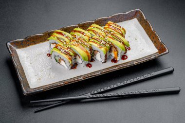 Bir tabakta avokado, sos ve susamlı suşi ruloları. Suşi dürümleri avokado dilimleri, sos ve susam tohumlarıyla bir tabağa konur..