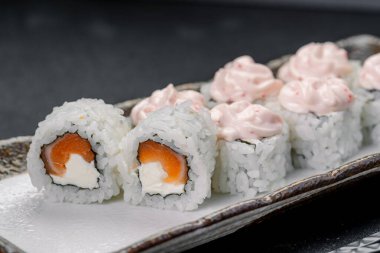 Siyah tabakta servis edilen somon ve krem peynirli suşi ruloları. Somon ve krem peynirle dolu suşi ruloları pembe soslu siyah bir tabakta düzenlenir..