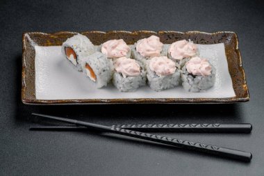 Suşi tabakta yuvarlanıyor ve yanında çubuklar var. Suşi dürümleri siyah yemek çubuklarıyla beyaz bir tabakta otururlar..