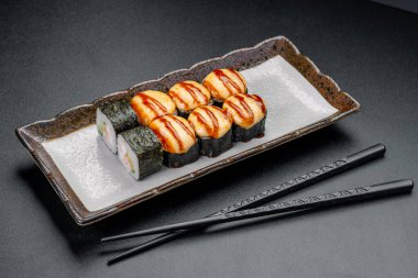 Suşi ruloları, yemek sırasında yanında çubuklarla siyah bir tabakta servis edilir..