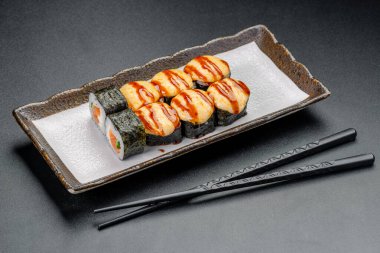 Bir tabakta sunulan suşi dilimleri yemek çubuklarıyla zevke getirilmeye hazır. Suşi ruloları, üzerinde sos ve yanında yemek çubukları olan bir tabakta güzelce düzenlenir..