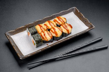 Suşi ruloları soslu ve çubuklu bir tabağa konur. Suşi ruloları üzerine sos serpiştirilmiş bir tabağa konur. Çubuklar yanına yerleştirilir..