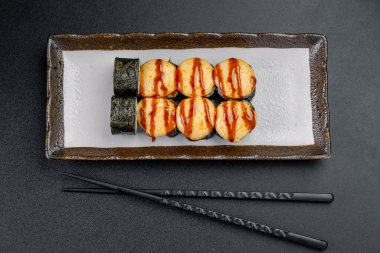 Suşi, masada çubuklarla siyah bir tabakta servis edilir. Yanında çubuklar olan dikdörtgen bir tabağa yerleştirilmiş suşiyle hazırlanmış yiyecekler..