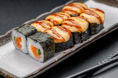 Restoran masasında soslu ve çubuklu suşi servis edilir. Dikdörtgen bir tabakta suşi ruloları çeşitli taze malzemeler ve soslar gösterir..