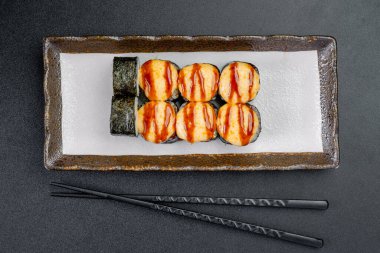 Lokantada yanında çubuklarla servis edilen suşi ruloları. Bir tabakta düzgünce sıralanmış suşi ruloları var..