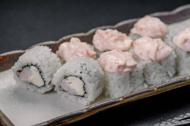 Restoran ortamında bir tabakta servis edilen kremalı soslu taze suşi ruloları. Kremayla doldurulmuş suşi ruloları ve pirinç dekoratif bir tabakta servis edilir..