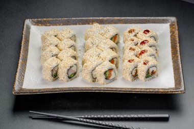 Yemek deneyimi için yemek çubuklarıyla servis edilen bir tabakta suşi yuvarlanıyor. Suşi ruloları beyaz bir tabakta güzelce düzenlenir..