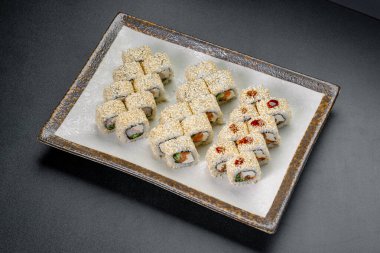 Öğle yemeği için bir restoranda kare tabakta suşi ruloları servis ediliyor. Kare tabakta susam tohumlarıyla kaplı çeşitli suşi ruloları var..