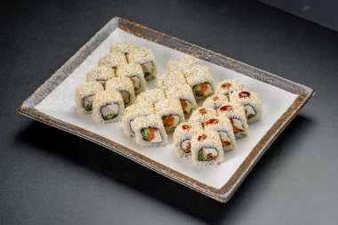 Basit bir restoranda gri bir tabakta suşi ruloları servis edilir. Çeşitli malzemelerle dolu suşi ruloları gri bir tabakta güzelce sıralanır..